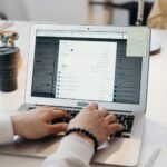 Interface do Google Sheets com colunas de um CRM e ícones de email, representando automação.