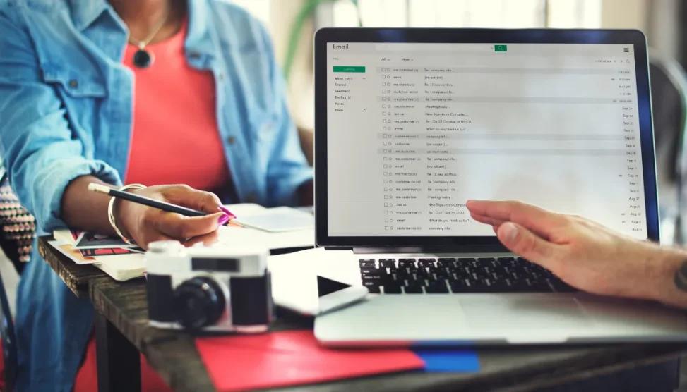 Mão digitando um e-mail em um notebook, com ícones de envelopes e gráficos de crescimento ao redor, simbolizando a comunicação e o sucesso na contabilidade.