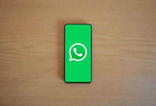 Mãos digitando em um celular com o logo do WhatsApp, conectando empresas em um ambiente corporativo
