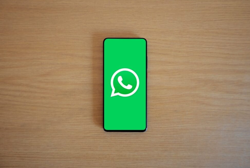 Mãos digitando em um celular com o logo do WhatsApp, conectando empresas em um ambiente corporativo