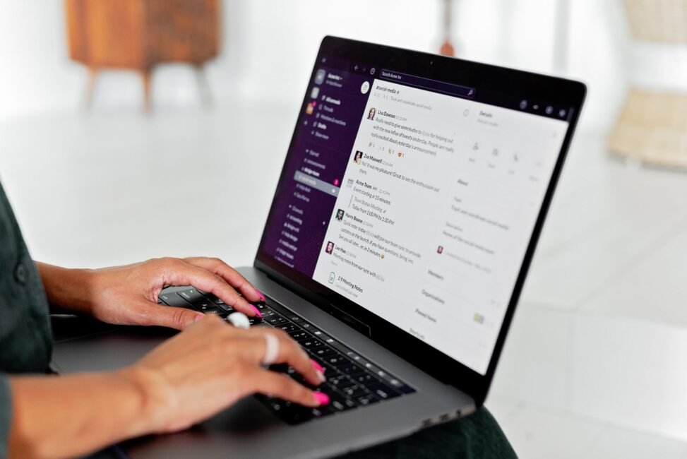 Pessoa utilizando um laptop com ícones de e-mail e validação, simbolizando a busca e verificação de endereços corporativos.